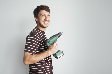 Young handsome guy with a screwdriver is drilling a white wall in a new apartment doing repairs.