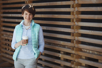 A young pretty woman in a blue jacket is drinking coffee.