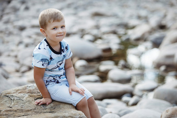 Blond boy in a blue t-shirt is playing with gray stones in a city park.