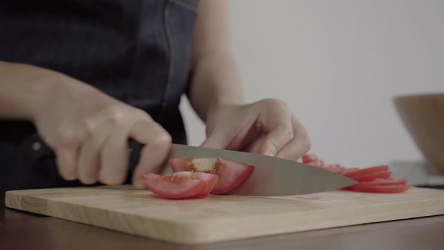 Close up of chief woman making salad healthy food and chopping tomato on cutting board in the kitchen.