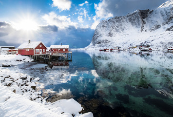 Famous tourist attraction of Reine in Lofoten, Norway with red rorbu houses water reflection on sunshine day.