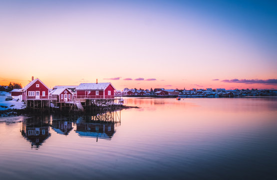 Famous tourist attraction of Reine in Lofoten, Norway with red rorbu houses water reflection at sunrise.