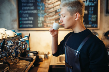 Young barista tastes fresh prepared coffee in cafe