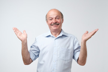Fototapeta premium Indoor portrait of confused senior man in blue shirt showing I have no idea gesture