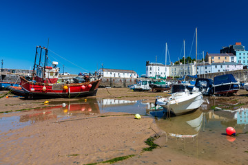 Colorful fishing and pleasure boats aground on the sand in Tenby harbour at low tide