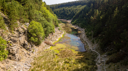 Fototapeta na wymiar Aerial drone view of a shallow lake inside a small canyon surrounded by green forest and cliffs (Tirpentwys and Blaencuffin, Wales)