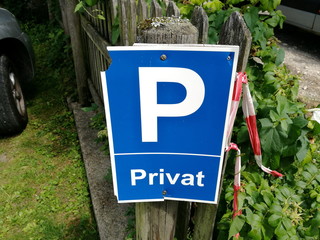 Blaues Verkehrsschild vor einem Privatparkplatz an der Einfahrt zu einem Grundstück mit Garten im...