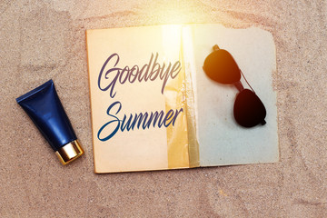 handwriting goodbye summer in old book with  blue cream tube and black sunglasses  above sand