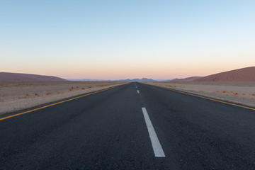 Fototapeta na wymiar Straight road though desert dunes towards sunset mountains, Sossusvlei, Namib desert, Naukluft National Park, Namibia