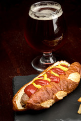 Ketchup and mustered added to a dog in a pretzel bun with a beer