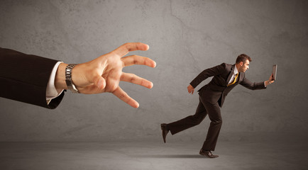 Young miniature businessman running from a big hand with grey background