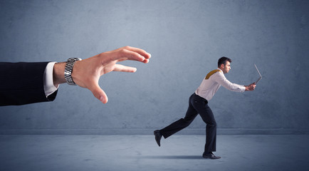 Young miniature businessman running from a big hand with blueish background