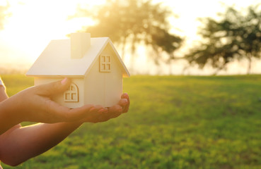 Image of woman holding small wooden house outdoors at sunset light.