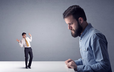 Young professional businessman being angry with an other miniature businessman in front of a grey background