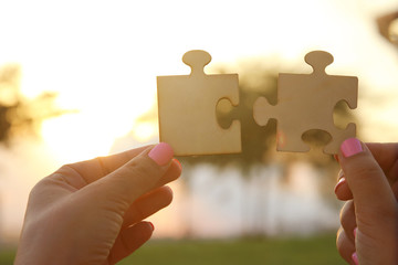 Concept image of a woman hands holding two pieces of a puzzle in front of the sun. Sunset time with lens flare. creativity and connectivity idea.