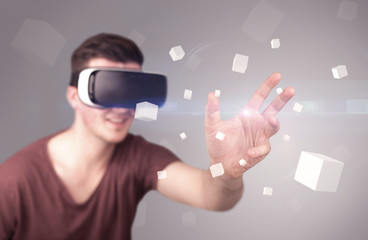 Young impressed man wearing virtual reality goggles with grey cubes around him 
