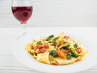 Italian pasta with tomatoes and a glass of wine, on a wooden background
