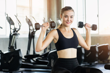 Muscular young woman with beautiful  body doing exercises with dumbbell. Sporty girl lifting weights in gym.