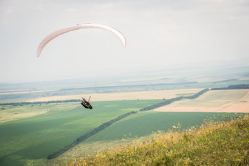 White orange paraglide with a paraglider in a cocoon against the background of fields of the sky and clouds. Paragliding Sports