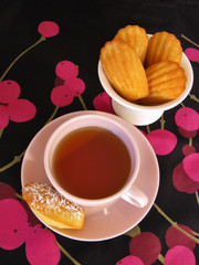 Classic shell-shaped French madeleines and cup of tea in retro china on cherry print tablecloth