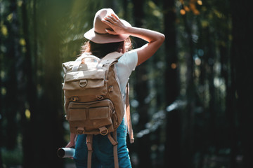 Lonely woman traveling among forest with backpack. Young traveler wearing hat and hold directional map in hand