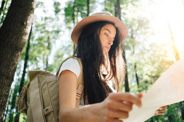 Pensive brave woman with backpack traveling alone among trees on outdoors. Young traveler girl...
