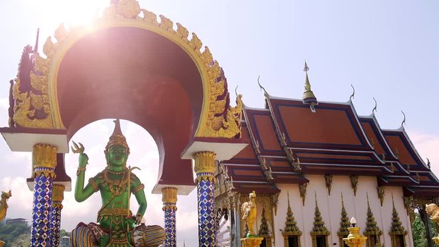 Shrine dedicated to Shiva with beautiful statue depicting him and Buddhist ceremonial hall illuminated by bright sun shining on background. Wat Plai Laem temple complex, Koh Samui, Thailand.