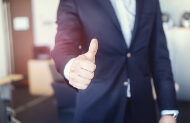 Closeup shot of a businessman in the office showing thumbs up. Success