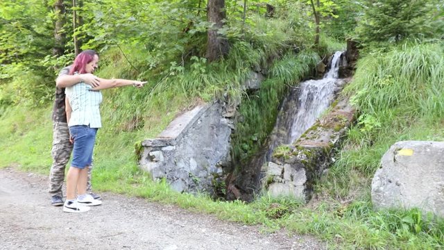 coppia si ferma a guardare una piccola cascata in montagna