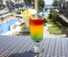 Bright cocktail with umbrella on the background of the pool