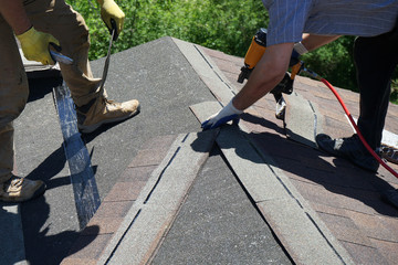 Roofer builders installing Asphalt Shingles or Bitumen Tiles on a roof of a new house.