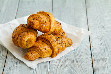 three croissant with a handful of seeds lying on a white paper on wooden grey background