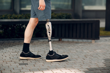 Disabled young man with foot prosthesis walks along the street.