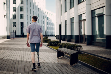 Disabled young man with foot prosthesis walks along the street. - obrazy, fototapety, plakaty