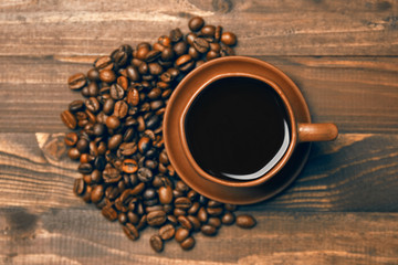 A cup of coffee and coffee beans on a brown wooden background, top view