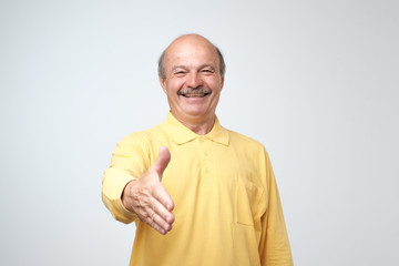 You are welcome concept. Cheerful mature man in yellow t-shirt shirt gesturing welcome sign and smiling