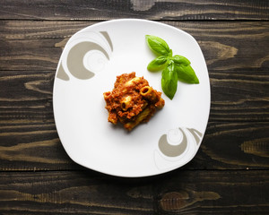 pasta with tomato sauce and basil on white plate on wooden background - top view