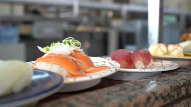 Close-up Sushi and Sashimi on Conveyer Belt. Dishes of Sushi and Sashimi rolling on conveyer belt. Shallow depth of field. Blurred movement in the background.