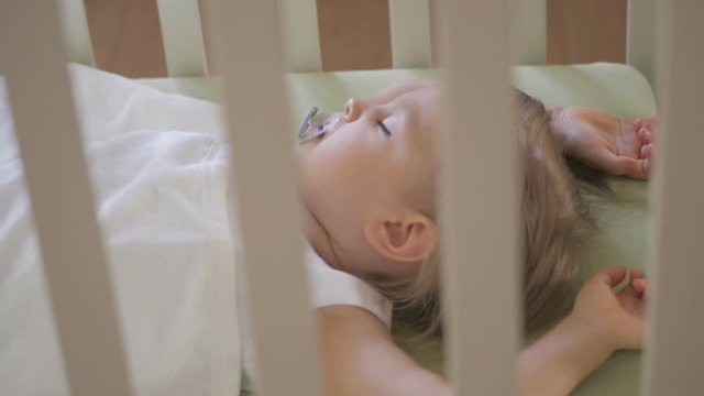 A little girl is sleeping in a baby crib with a pacifier in her mouth