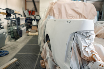 Garage painting car service. section of the car is covered with primer. vehicle is covered with protective paper. Repairing car body work after the accident by working sanding primer before painting.