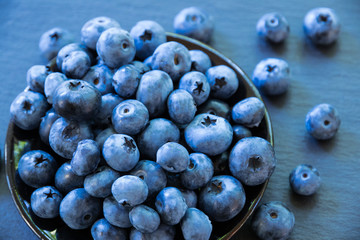 blueberry on a stone table. A glass vase with blueberry berries is on a dark stone table top. Spilled summer berries on the table. Healthy product.
