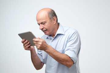 Mature european man using a digital tablet. He is puzzled and confused.