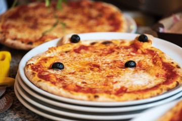 Kinder Margarita Pizza mit Gesicht aus dem Pizzaofen auf einem Teller und in einer Schachtel