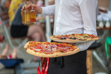 Italienischer Kellner bedient auf der Terrasse  mit zwei Pizza in der Hand 