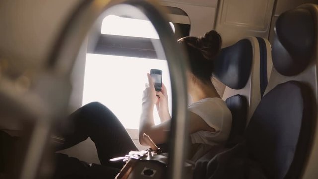 Beautiful happy smiling Caucasian girl taking a smartphone picture enjoying traveling on modern train window seat.