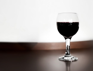 One glass of red wine wooden table and blurred white wall background. Alcohol drink on desk in room.