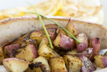 Plate of grilled sausage and red potatoes on white ceramic plate.  Crossed chives as garnish.