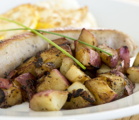 Plate of grilled sausage and red potatoes on white ceramic plate.  Crossed chives as garnish.