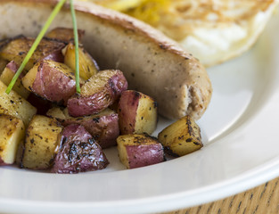 Plate of grilled sausage and red potatoes with fried eggs.