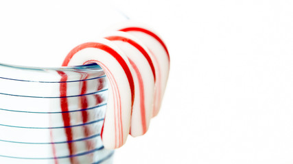 Candy canes hooked over the rim of a textured blue glass.  Bright white background.  High key.